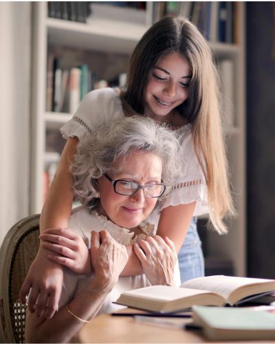 Une grand-mère assise lit sa biographie. Sa petite-fille est debout derrière elle et l'entoure de ses bras.